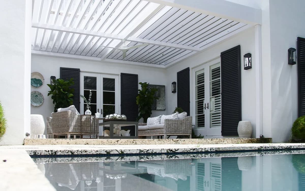 White wall-mounted Azenco R-BLADE louvered pergola integrated with a home's covered poolside patio