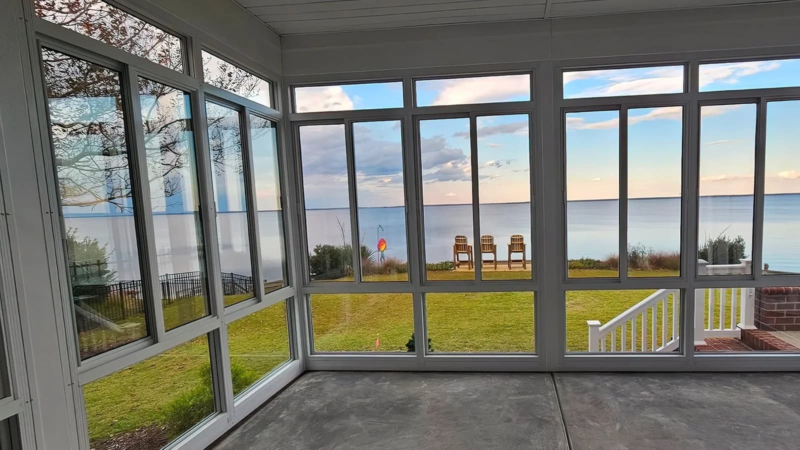 White aluminum-framed sunroom with tall windows overlooking a lawn and water