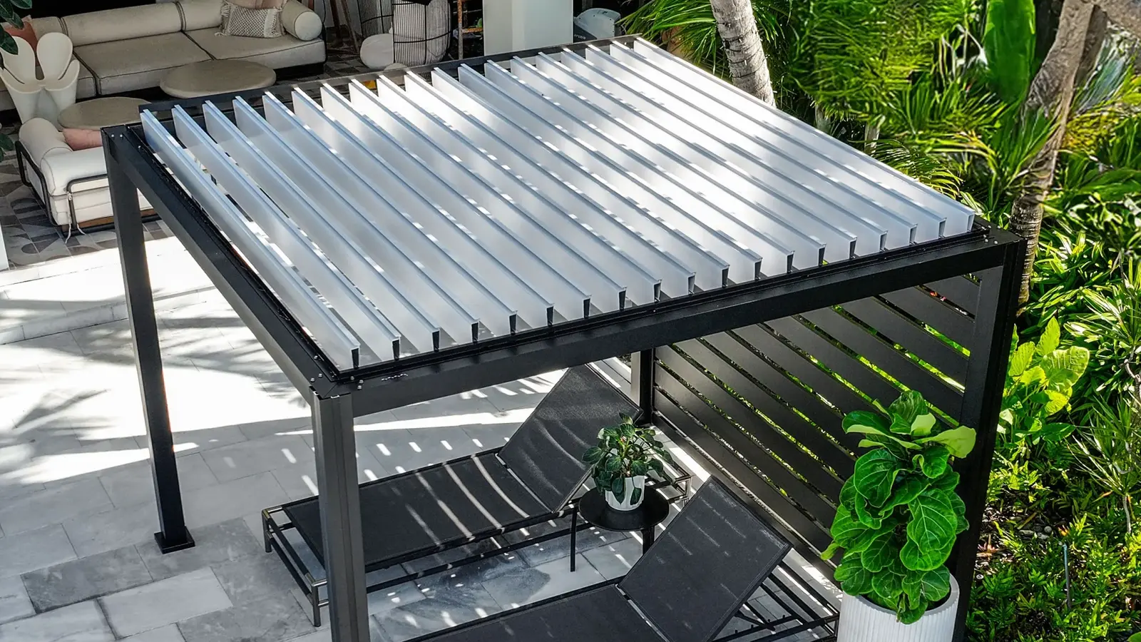 Black K-BANA pergola with white manual roof louvers above two lounge chairs