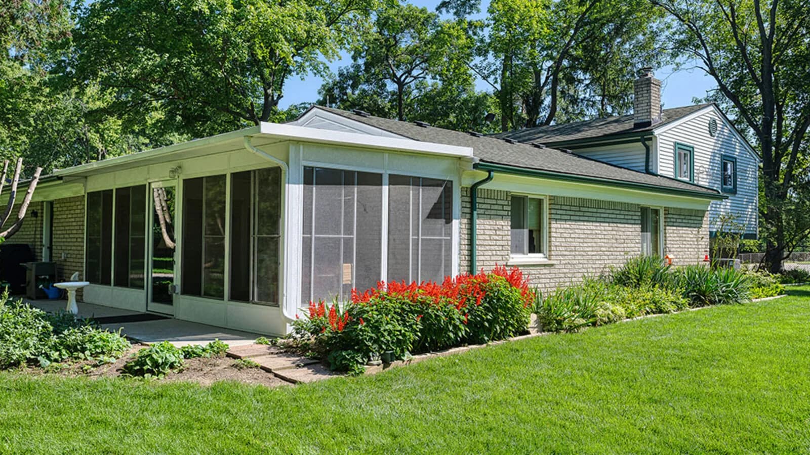 White aluminum screen room with dark mesh panels and a solid roof beside a brick home