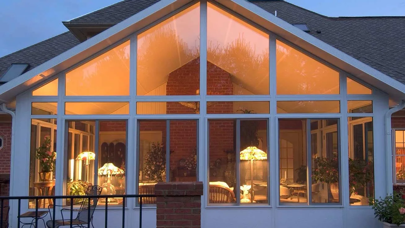 White aluminum sunroom with tall windows, upper transom glass, and solid lower wall panels