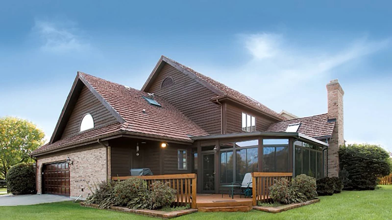 Bronze aluminum sunroom with a low-pitch roof attached beneath the eaves of a two-story home