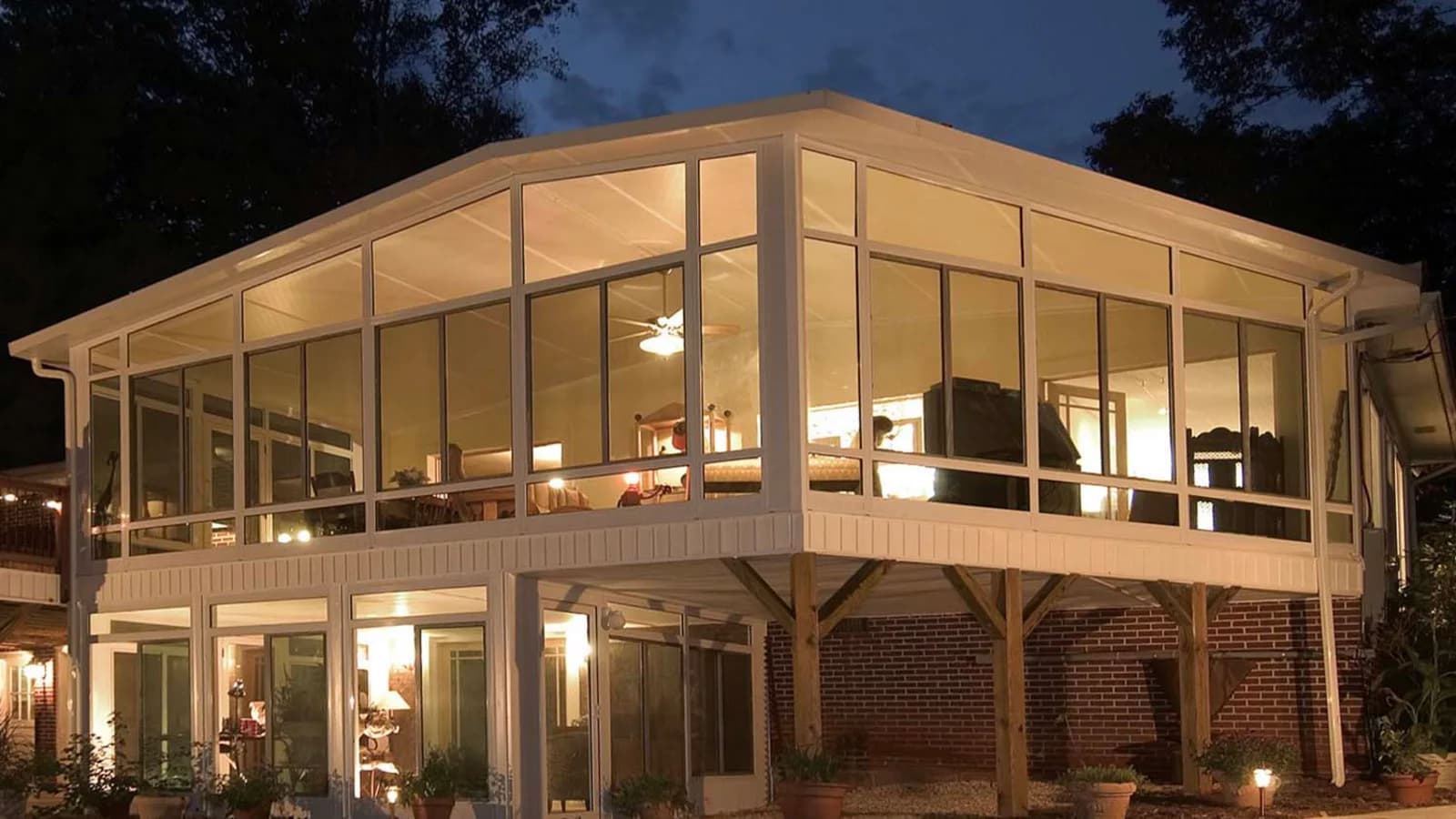 Elevated glass sunroom supported above a ground-level patio beside a brick home