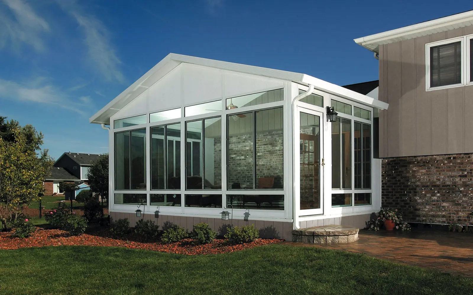 White glass-walled cathedral sunroom attached to a Charlotte-area home beside a landscaped lawn