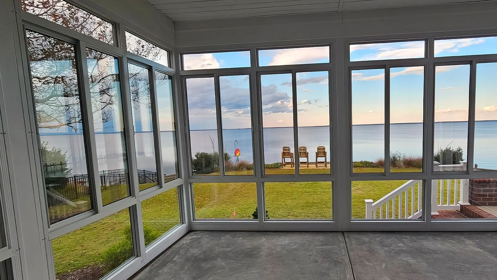White aluminum-framed sunroom with tall windows overlooking a lawn and water